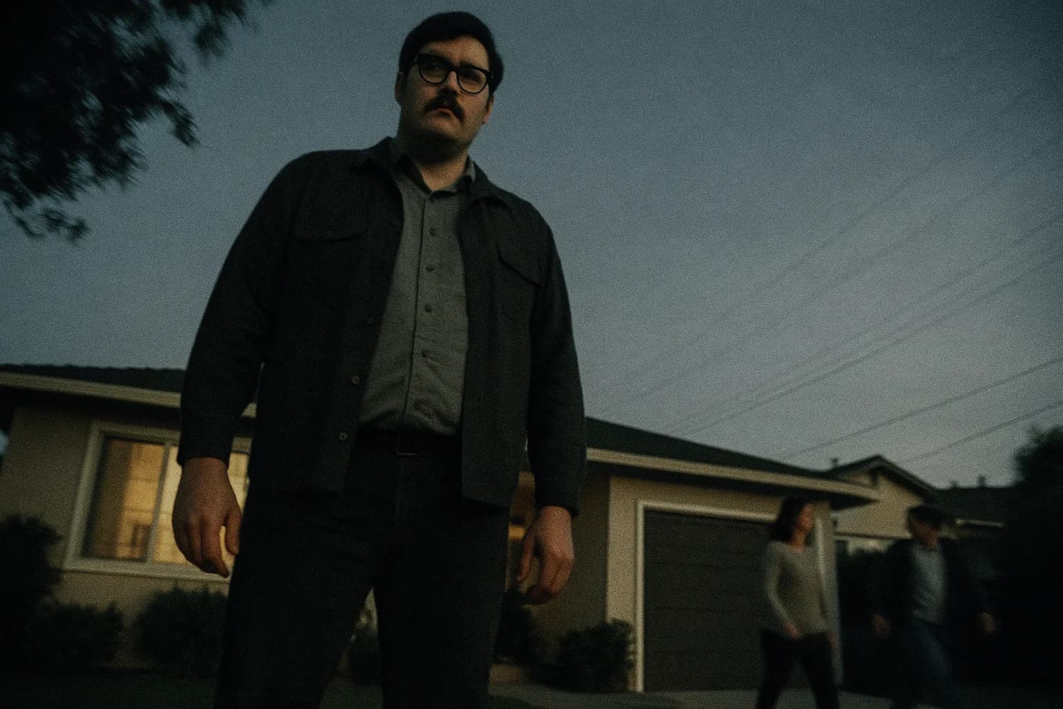 En skikkelse, der ligner Edmund Kemper, står udenfor et forstadshus i Californien, truende høj med et tomt blik, mens naboer går forbi uvidende, hvilket symboliserer de skjulte rædsler, der lurer under overfladen.