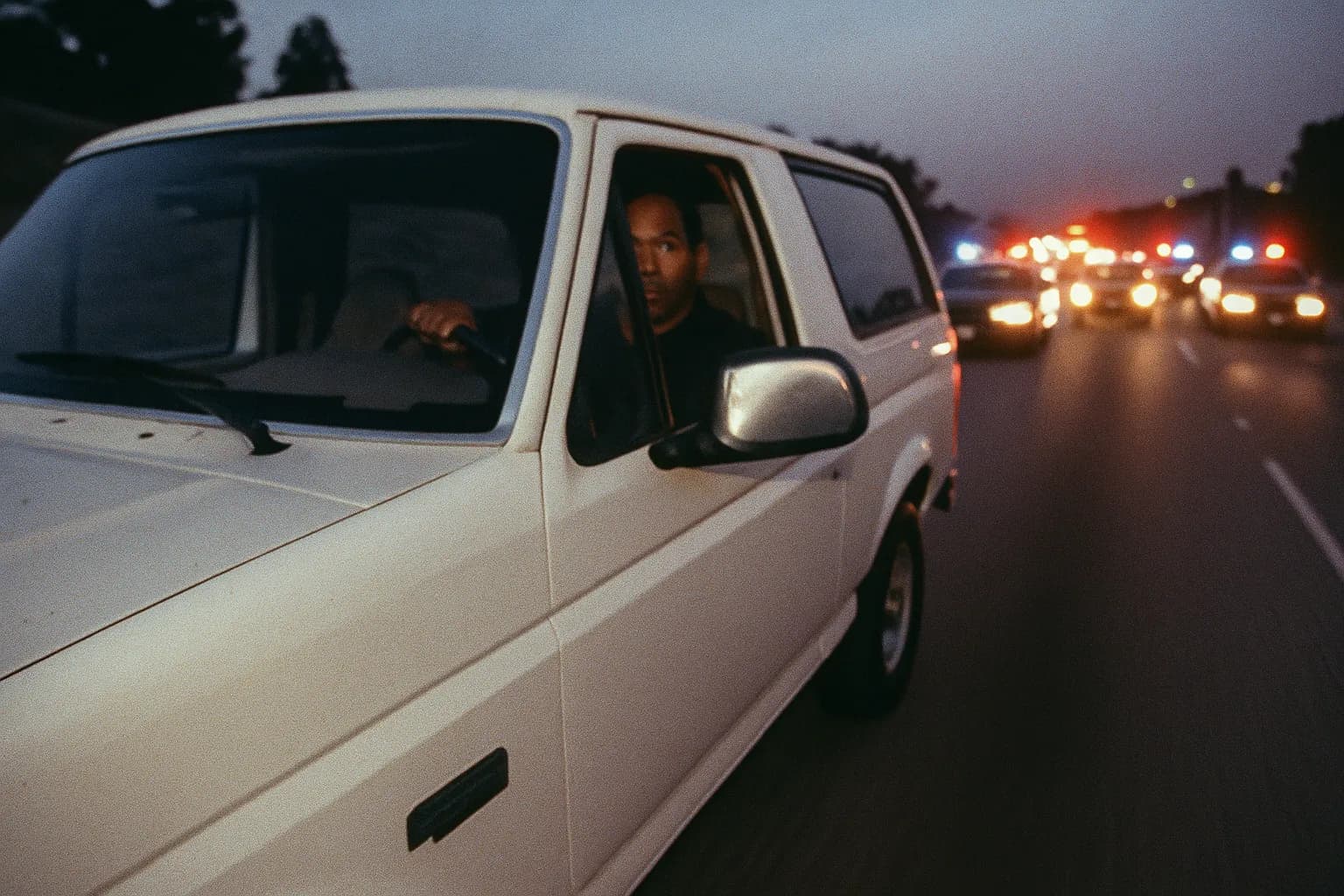En figur, der ligner O.J. Simpson, sidder i førersædet i en hvid Ford Bronco, omgivet af politibiler, under den berygtede langsomme jagt den 17. juni 1994.